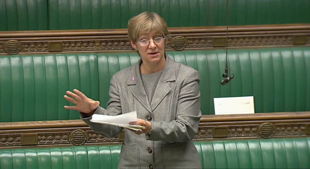 Rachel Squire wearing a grey suit standing with backdrop of green benches